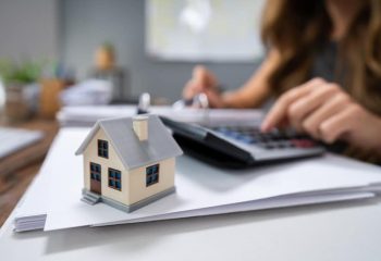 Close-up Of A Person Hand Calculating A Real Estate Property Tax On Wooden Desk