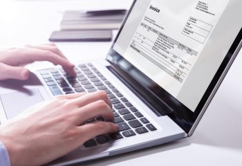 Close-up Of A Businessman's Hand Checking Invoice On Laptop