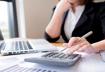 Asian female accountant or banker making calculations. Savings, finances and economy concept through a laptop.