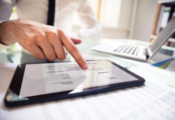 Close-up Of A Businessperson's Hand Analyzing Bill On Digital Tablet Over Desk