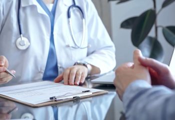 Doctor woman is writing something while consulting man patient on the glass desk and a clipboard in medical office. Medicine concept.