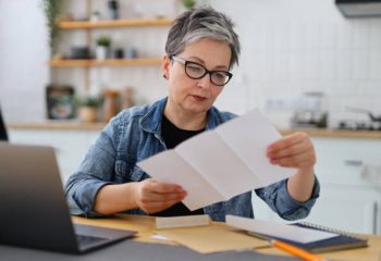 Serious mature woman in glasses reading the bill in the kitchen.