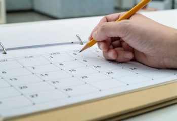 Woman hand with pencil writing on calendar page.