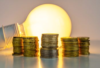 Lit light bulb with coins beside it. Increase in energy tariffs. Efficiency and energy saving.