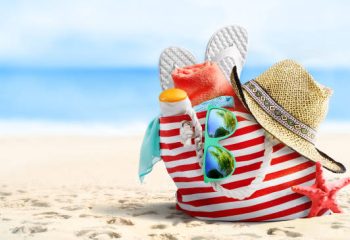 Summer vacations concept background. Beach bag, straw hat, flip flops, sunglasses and starfish on sandy beach and azure sea on background.