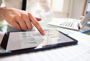Close-up Of A Businessperson's Hand Analyzing Bill On Digital Tablet Over Desk