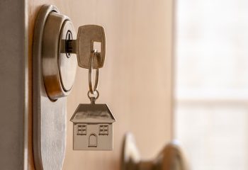 CLOSE UP OF KEY AND HOUSE KEYCHAIN ​​IN HIGH SECURITY DOOR LOCK. HOME INSURANCE CONCEPT. COPY SPACE.
