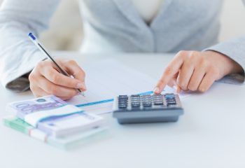 business, finance, tax and people concept - close up of woman hands counting euro money with calculator and tax report form