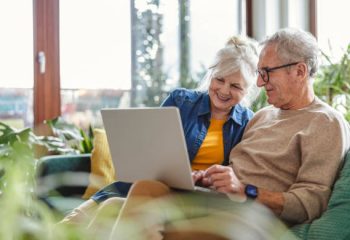 Senior couple using laptop while sitting on sofa in living room at home