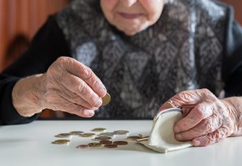 Elderly 95 years old woman sitting miserably at the table at home and counting remaining coins from the pension in her wallet after paying the bills.