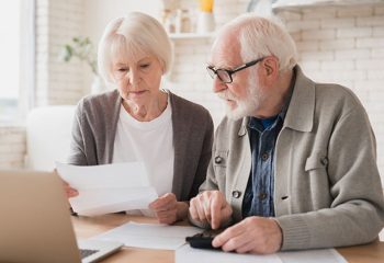 Serious caucasian old elderly senior couple grandparents family counting funds on calculator, doing paperwork, savings, paying domestic bills, mortgage loan, pension at home using laptop.