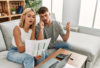 Young caucasian couple with serious expression controlling family economy using laptop and smartphone at home.
